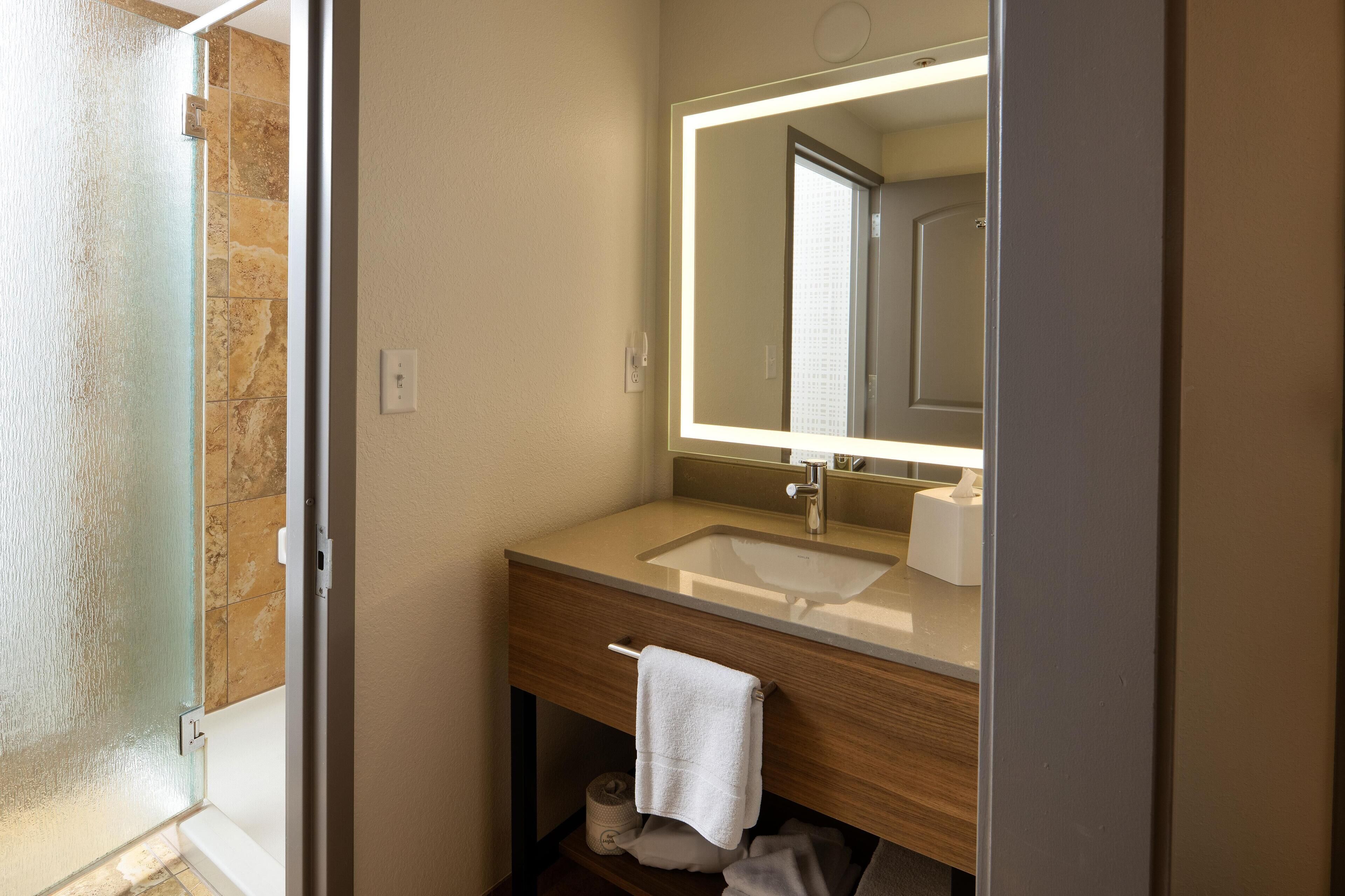 Un baño con lavamanos, espejo, toalla y papel higiénico.
