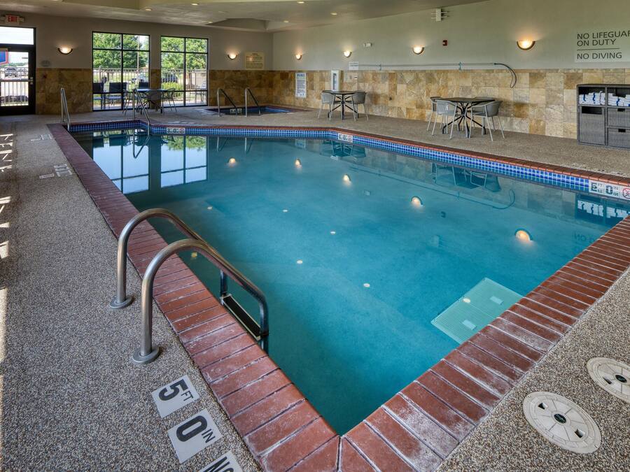 Una piscina interior con borde de azulejos, una estación de socorristas y un área de descanso con mesas y sillas.