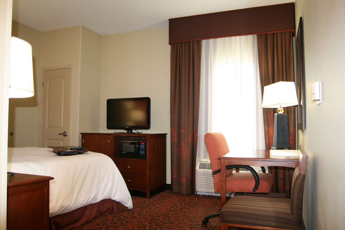 Een hotelkamer met een bed, een bureau met een computer, een televisie en een stoel.