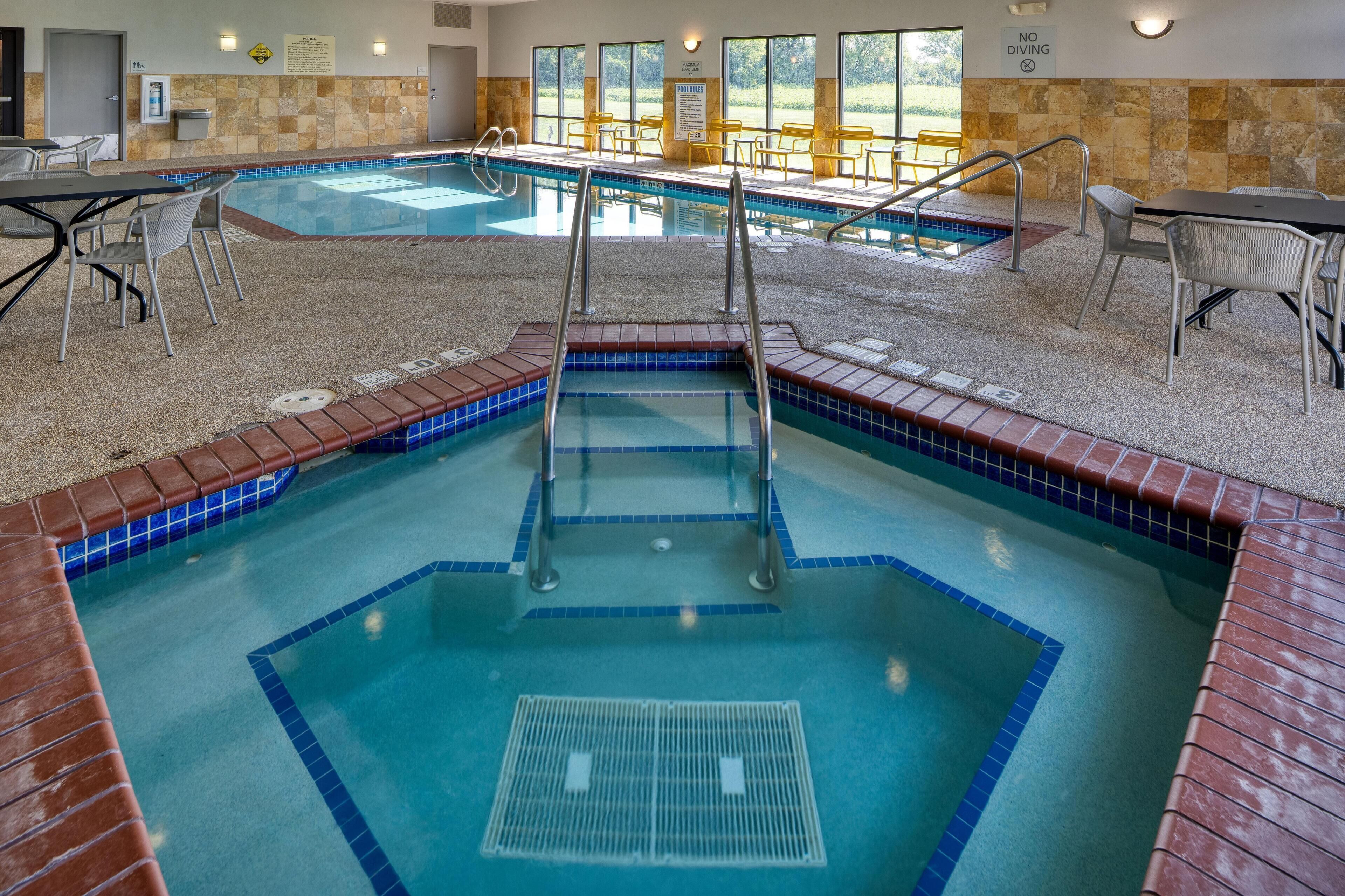 An indoor swimming pool with multiple lanes, safety railings, and a seating area with chairs.