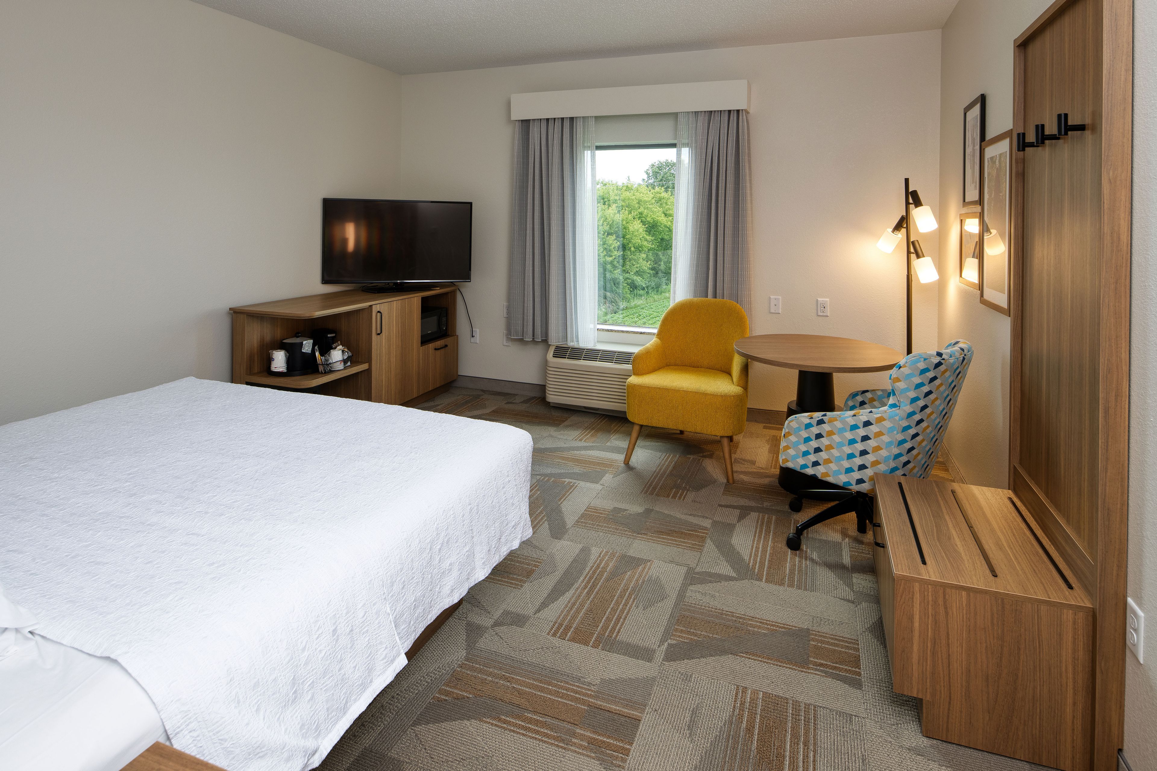 A hotel room with a bed, a television, a small table, a chair, and a window with curtains.
