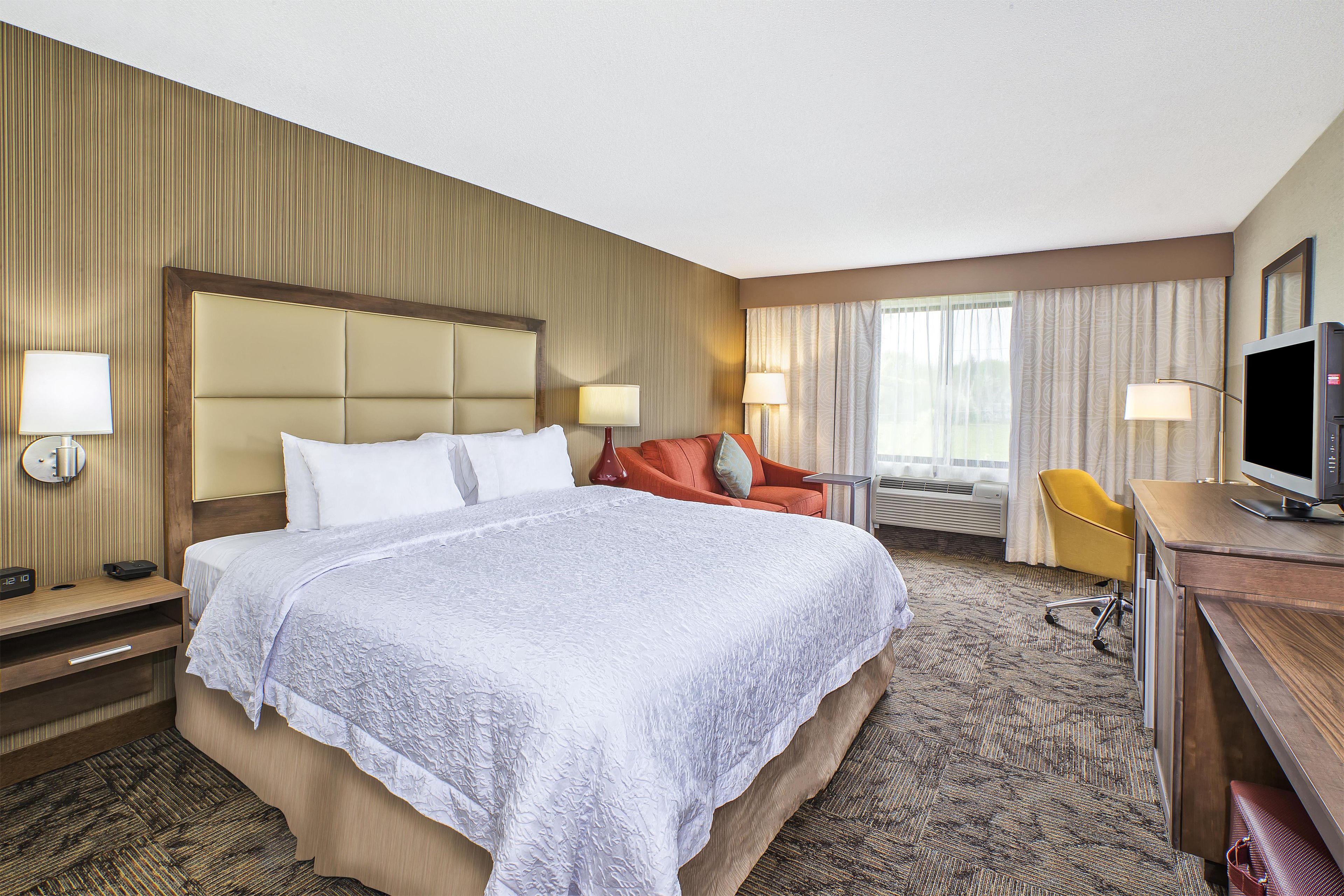 Habitación de hotel con una cama grande, un escritorio con televisor y una zona de estar con un sillón.