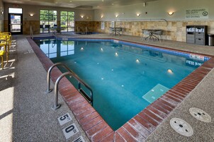 Una piscina interior con borde de azulejos, una estación de socorristas y un área de descanso con mesas y sillas.