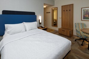 Habitación de hotel con una cama grande, un escritorio, una silla, un armario y un espejo.