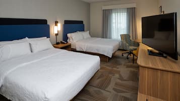 A hotel room with two beds, a desk with a television, a chair, and a window with curtains.