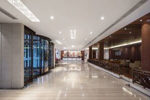 Een ruime lobby met een gepolijste marmeren vloer, een receptiebalie en een zithoek met een balustrade.