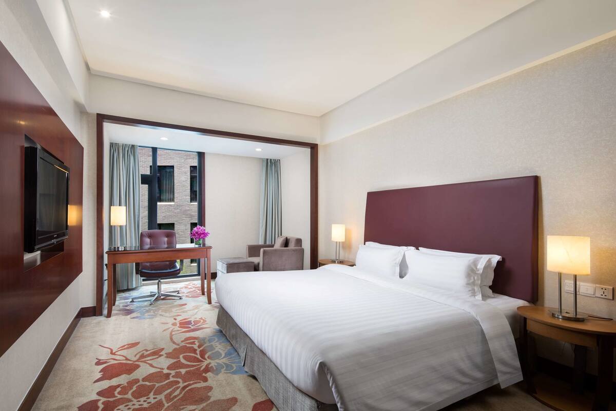 Hotelkamer met een groot bed, een televisie, een bureau met stoel en uitzicht op buiten.