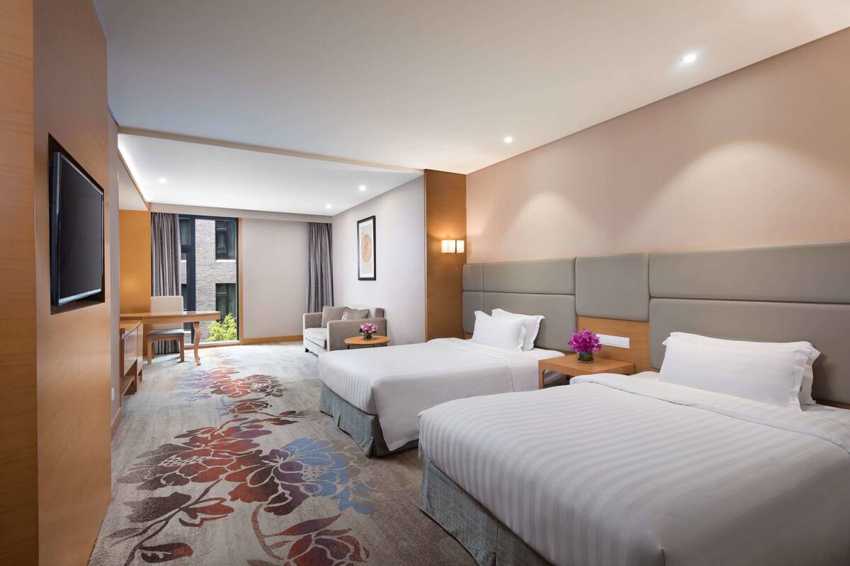 Een hotelkamer met twee bedden, een bureau, een stoel en een raam.
