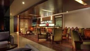 Um saguão de hotel moderno com área de bar, assentos e uma televisão visível.
