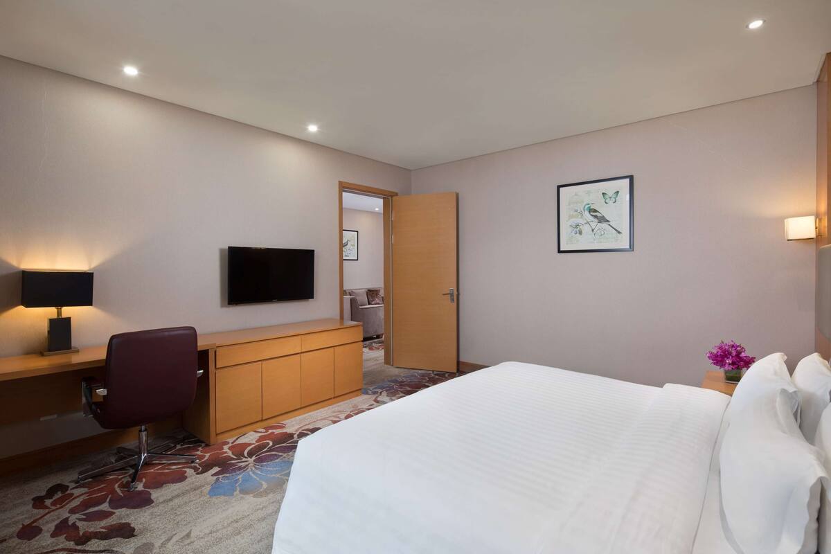 Een hotelkamer met een bed, bureau, stoel, televisie en een deur die naar een andere kamer leidt.