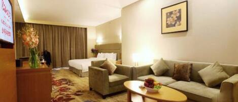 A hotel room with a bed, a sofa, a coffee table, and a desk with a vase of flowers.