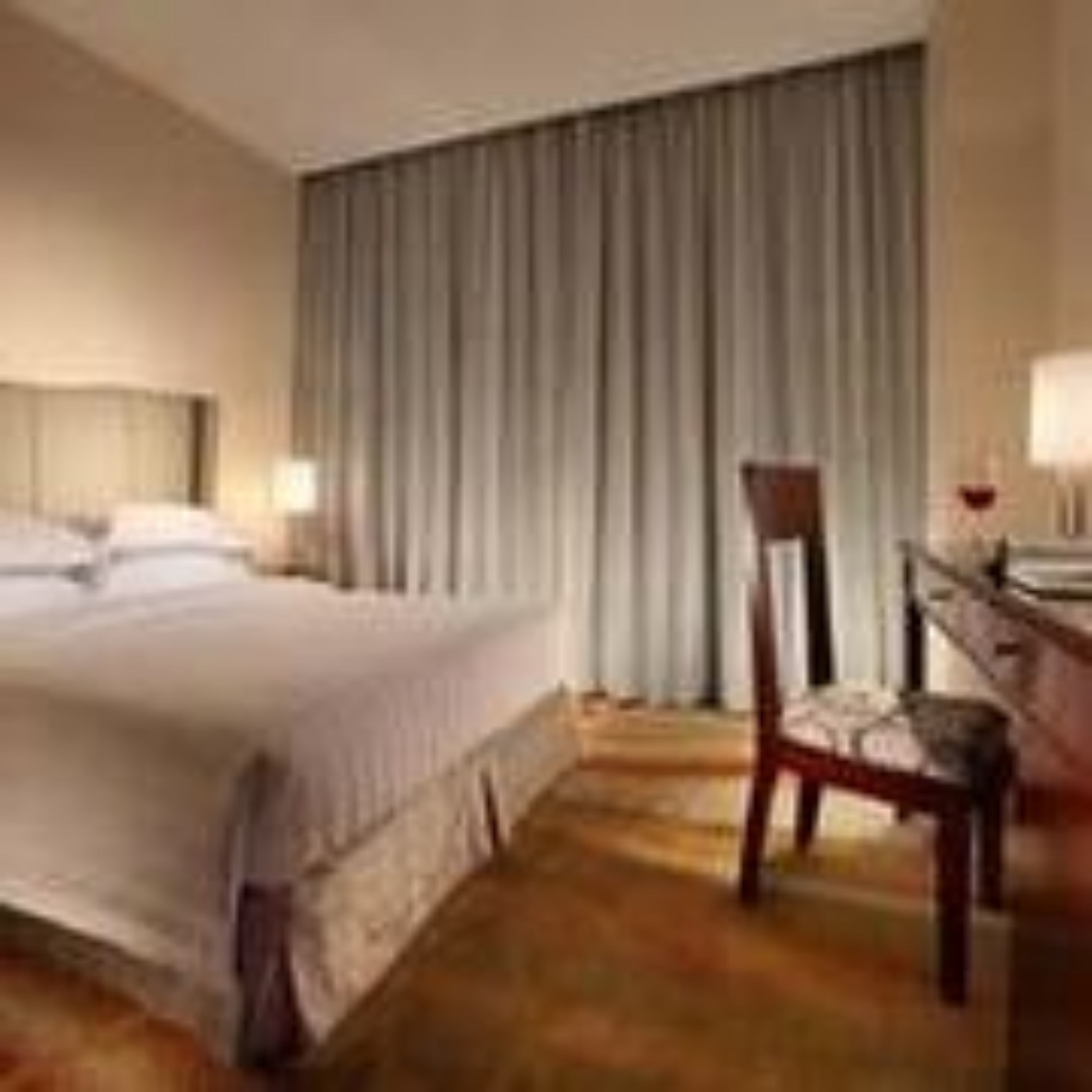 Habitación de hotel con una cama grande, un escritorio con silla y una ventana con cortinas.