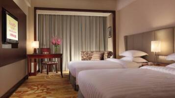 A hotel room with two beds, a desk with a chair, a television, and a window with curtains.