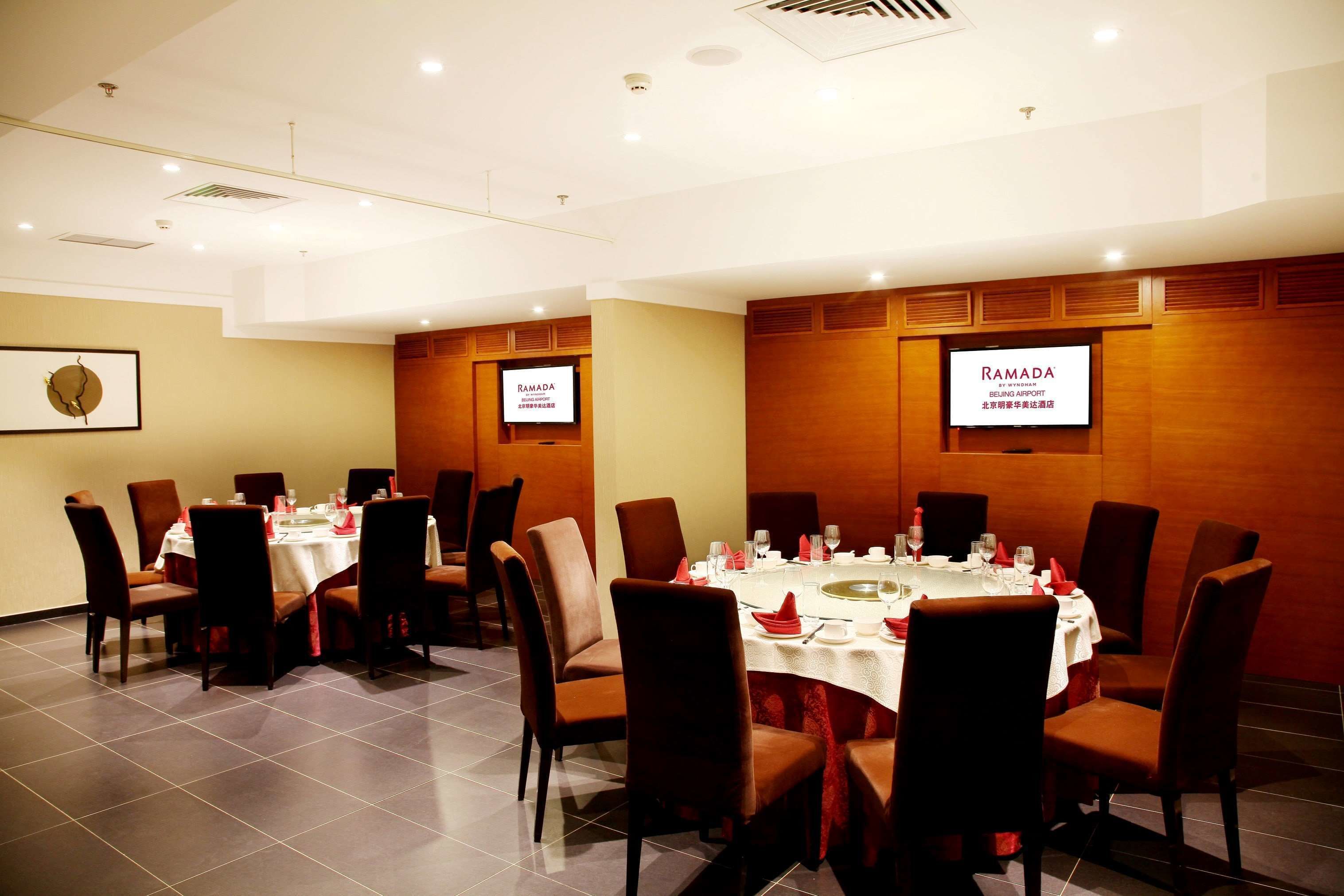 A conference room with round tables, chairs, and a large screen displaying "RAMADA".