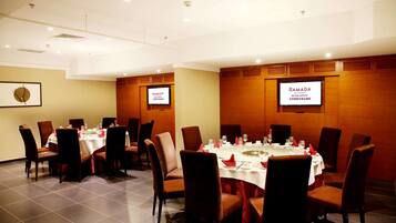 A conference room with round tables, chairs, and a large screen displaying "RAMADA".