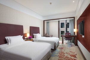 Habitación de hotel con dos camas, un escritorio, una silla, un televisor y vistas al exterior.