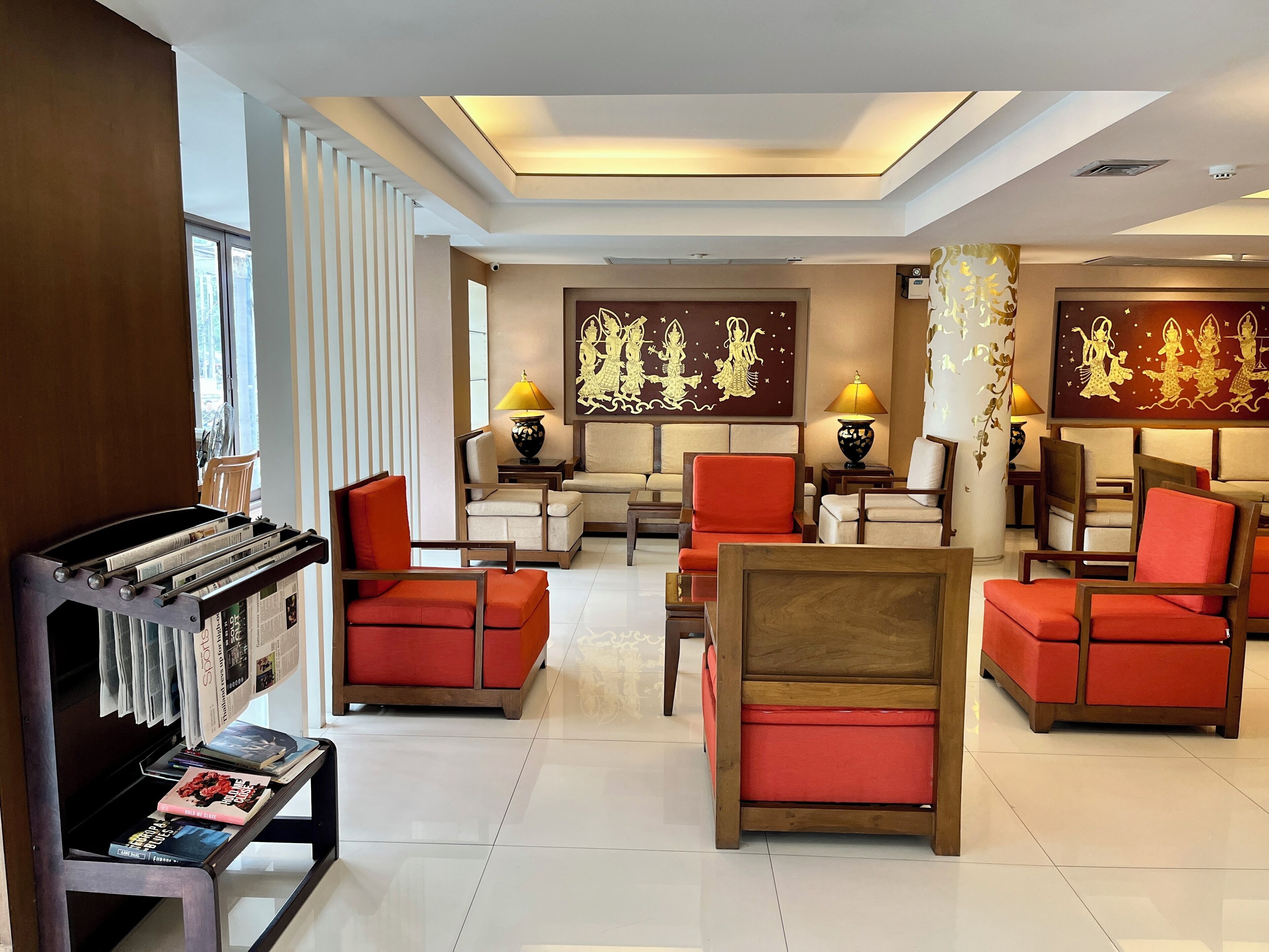 A hotel lobby with a modern design, featuring a mix of red and beige seating, decorative wall art, and a magazine rack.