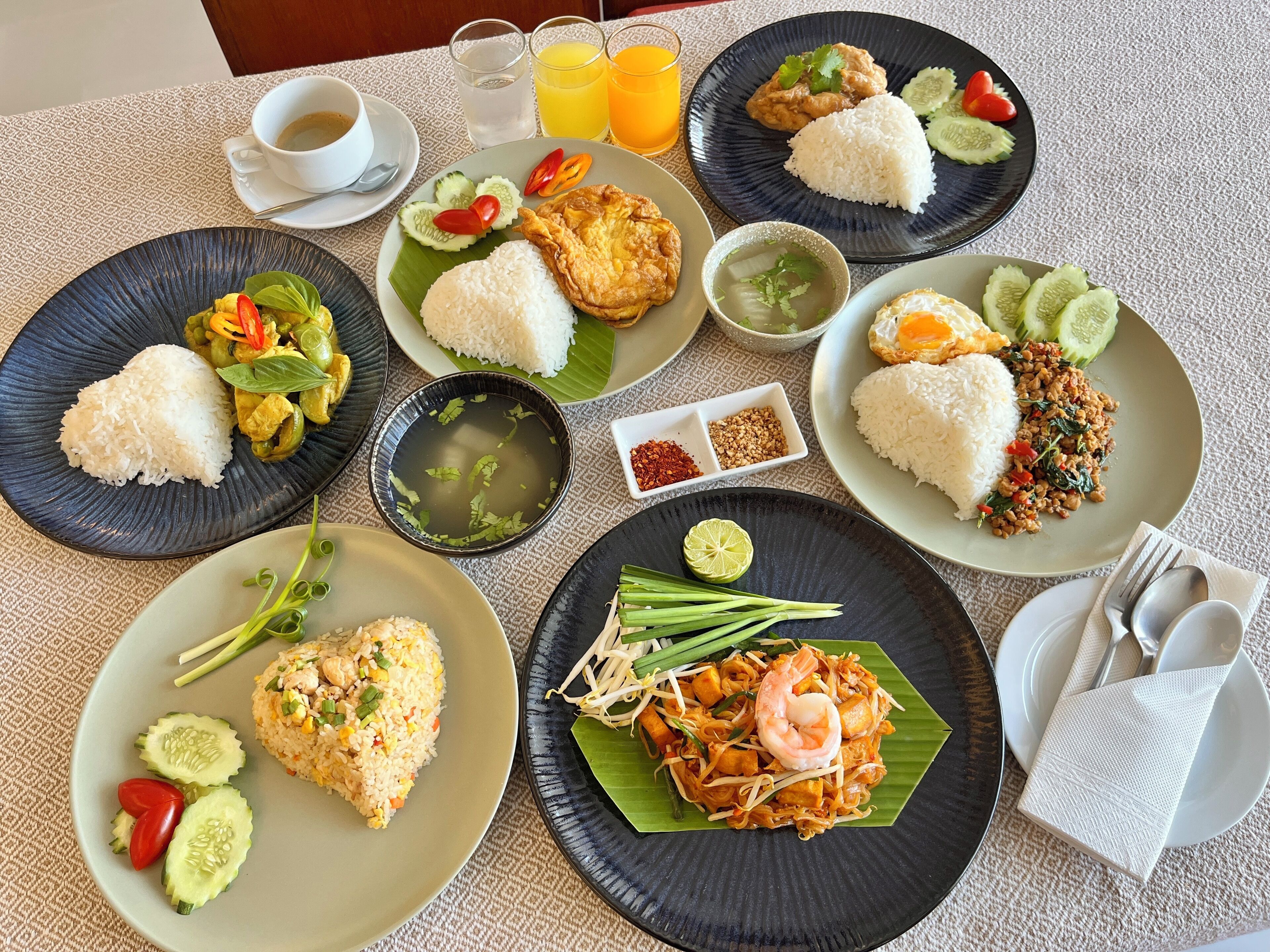 A table with various dishes including rice, fried chicken, and noodles, accompanied by drinks and condiments.