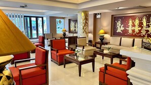 A hotel lobby with a reception desk, seating area with red chairs and tables, decorative wall art, and a large window providing a view of the outside. - Mariya Boutique Residence at Suvarnabhumi Airport (Bangkok)