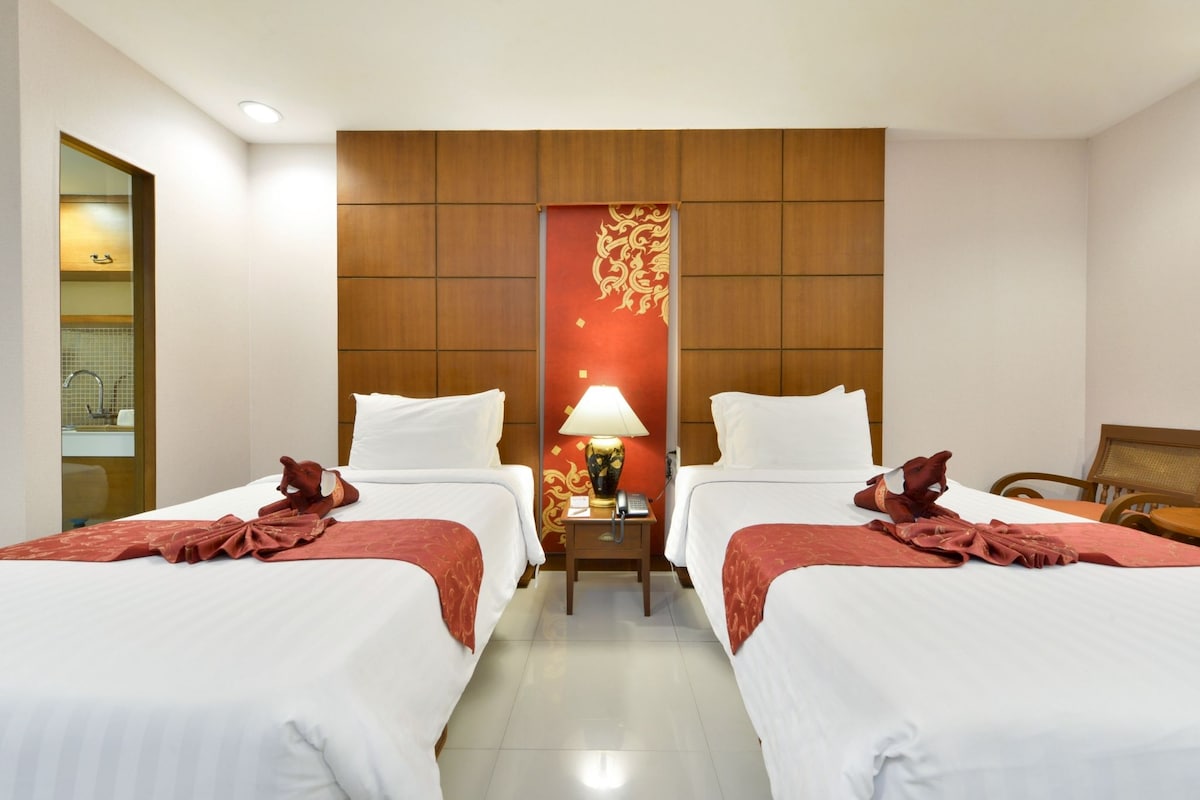 A hotel room with two beds, a nightstand with a lamp, and a decorative wall panel.
