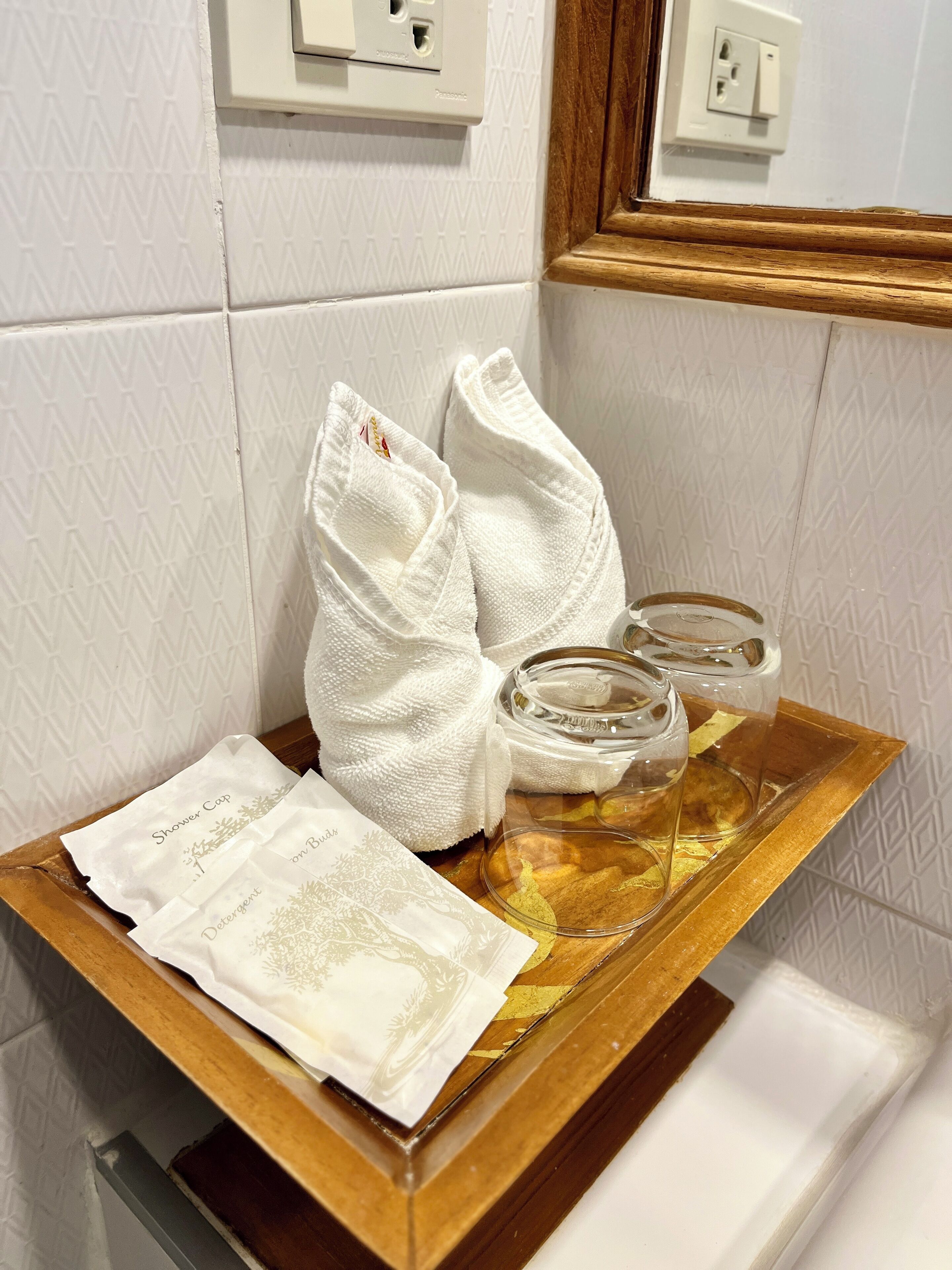 A bathroom with a wooden tray holding a towel, a glass container, and a paper towel dispenser.