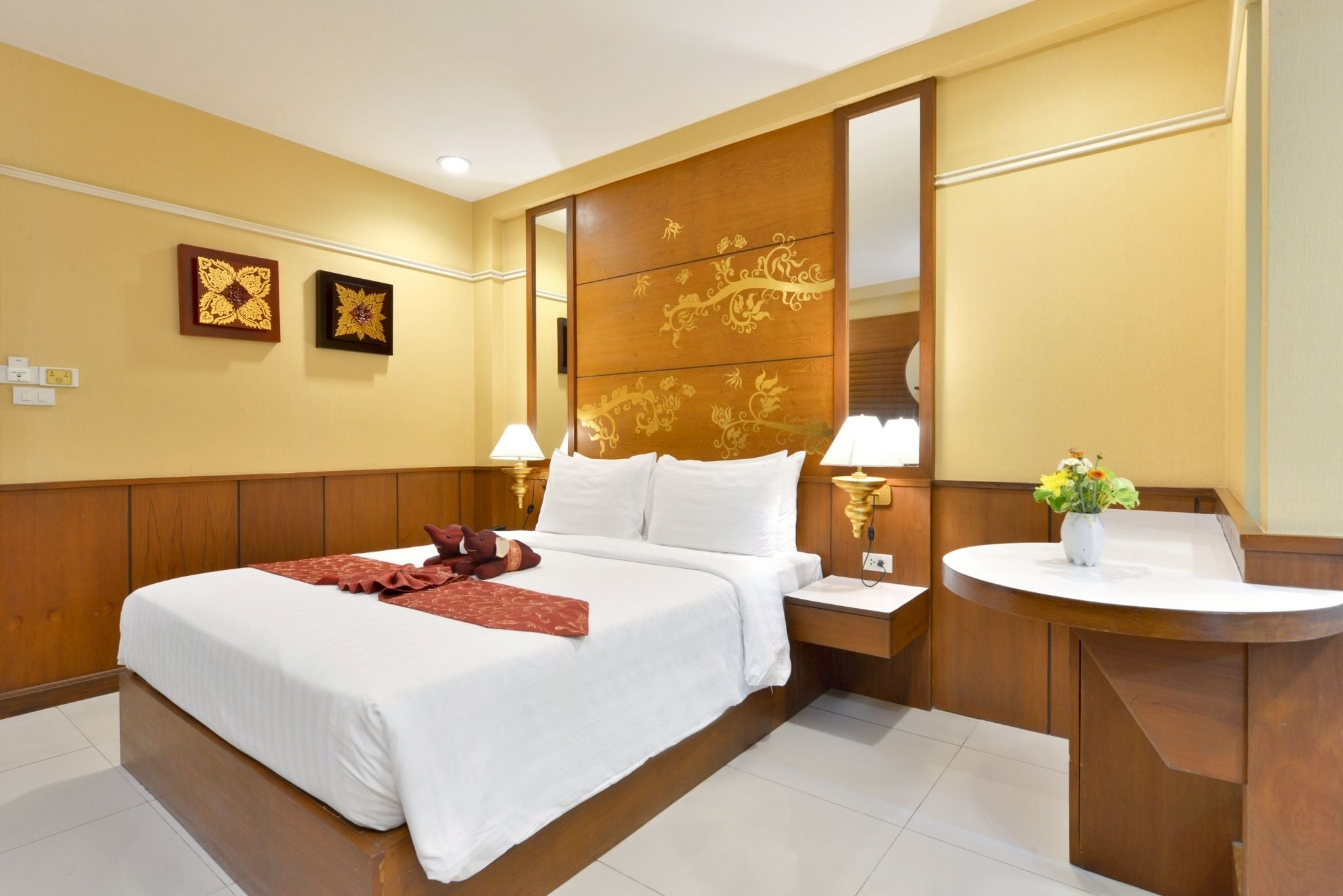 A hotel room with a large bed, bedside lamps, a wooden headboard, and a vanity with a mirror.
