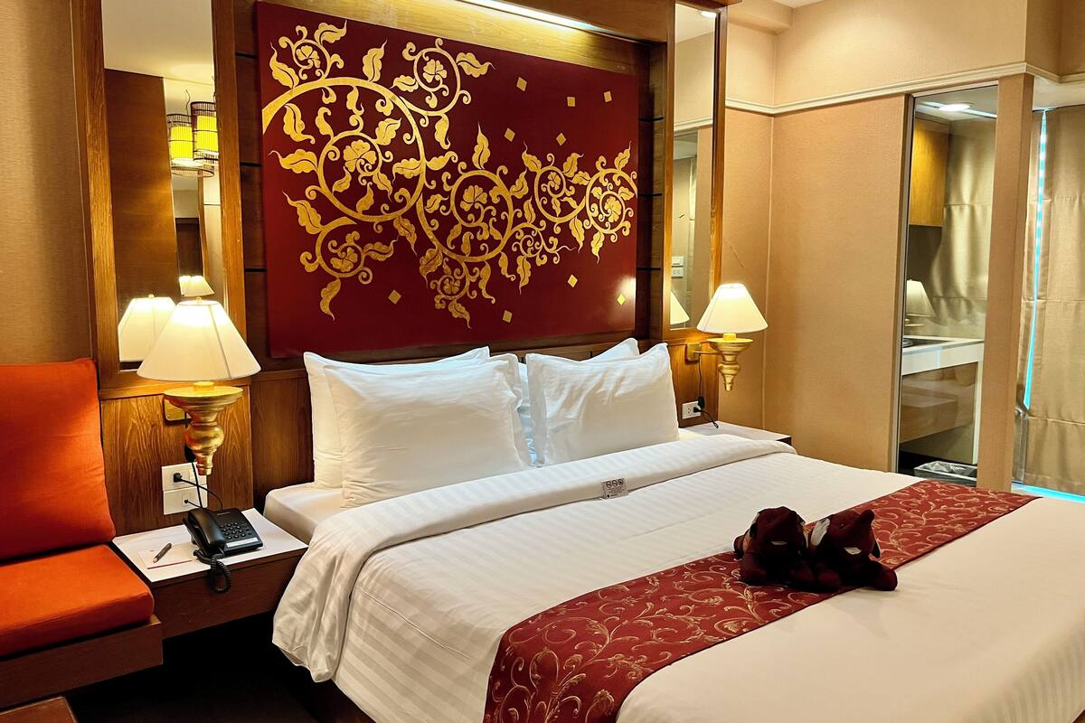 A hotel room with a large bed, two bedside lamps, a telephone, a nightstand, and a plush red chair.