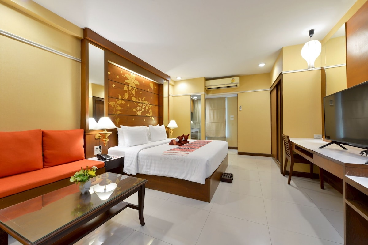 A hotel room with a bed, a sofa, a desk, and a television.