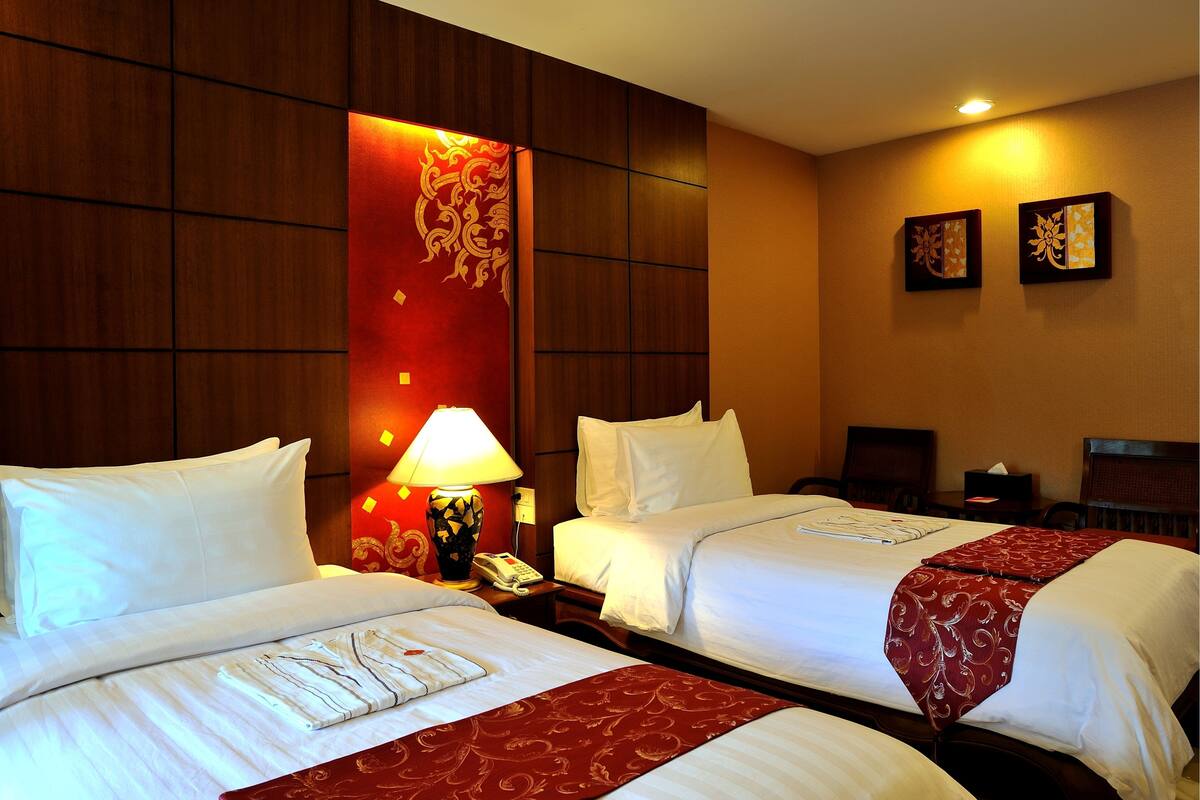 A hotel room with two beds, a nightstand with a lamp, a telephone, and a wall with two decorative pieces.