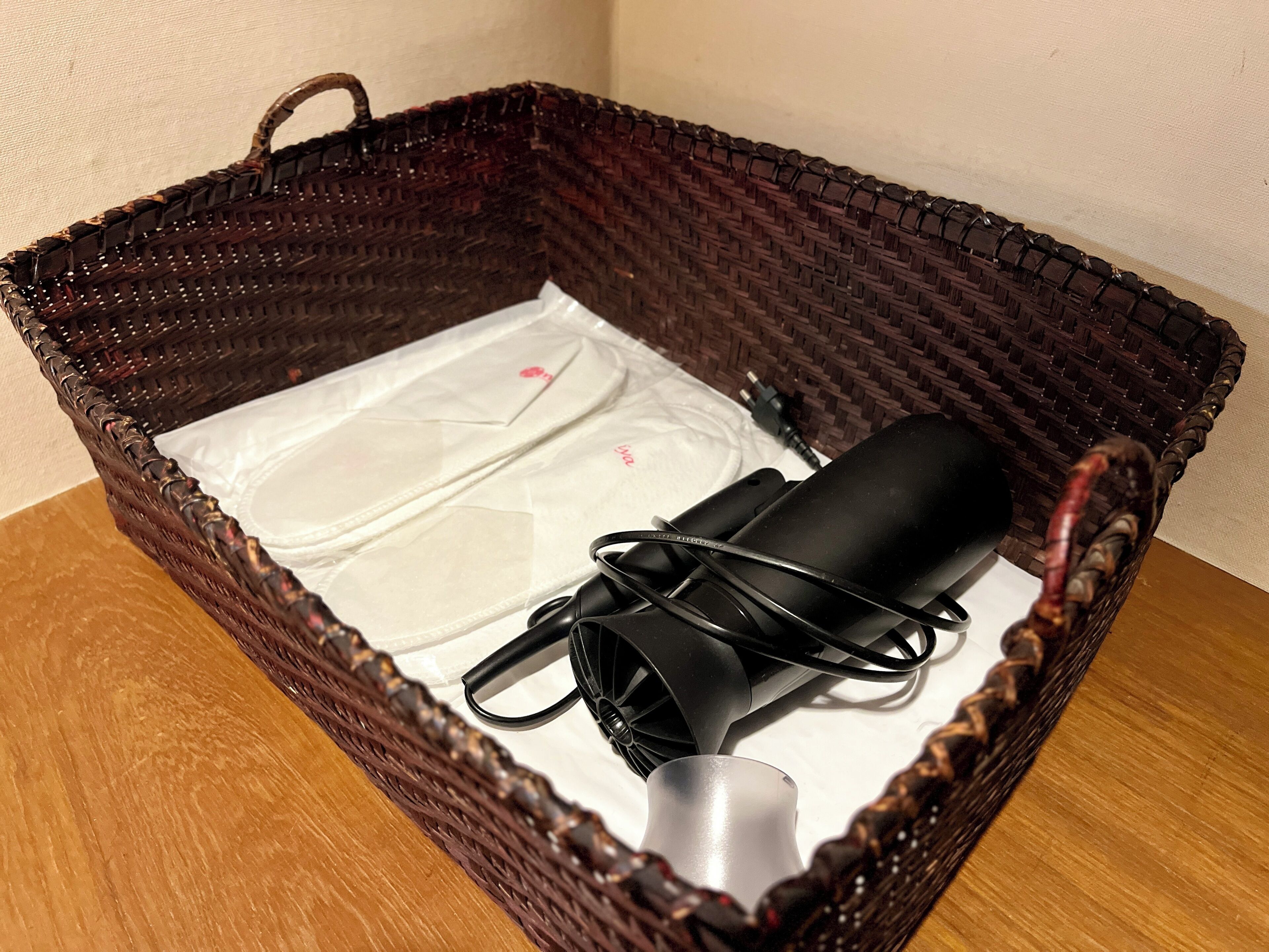 A wicker basket containing a white plastic bag, a black cylindrical object, and a black cable.