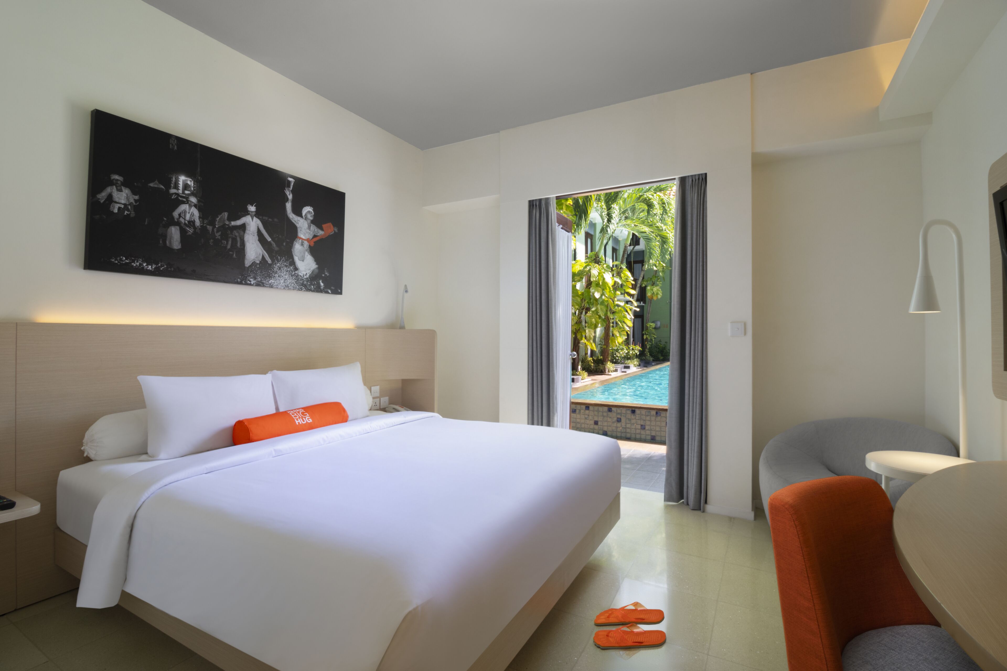 Une chambre d’hôtel moderne avec un grand lit, un tableau au mur, une vue sur une piscine extérieure et un coin salon.