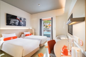 A hotel room with two beds, a desk with a chair, a TV, and a view of the pool area.