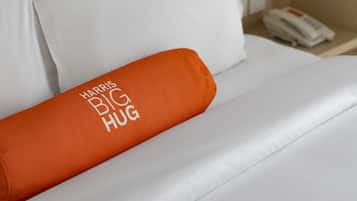 A hotel room with a bed featuring white bedding and an orange pillow with "HARRIS BIG HUG" text.
