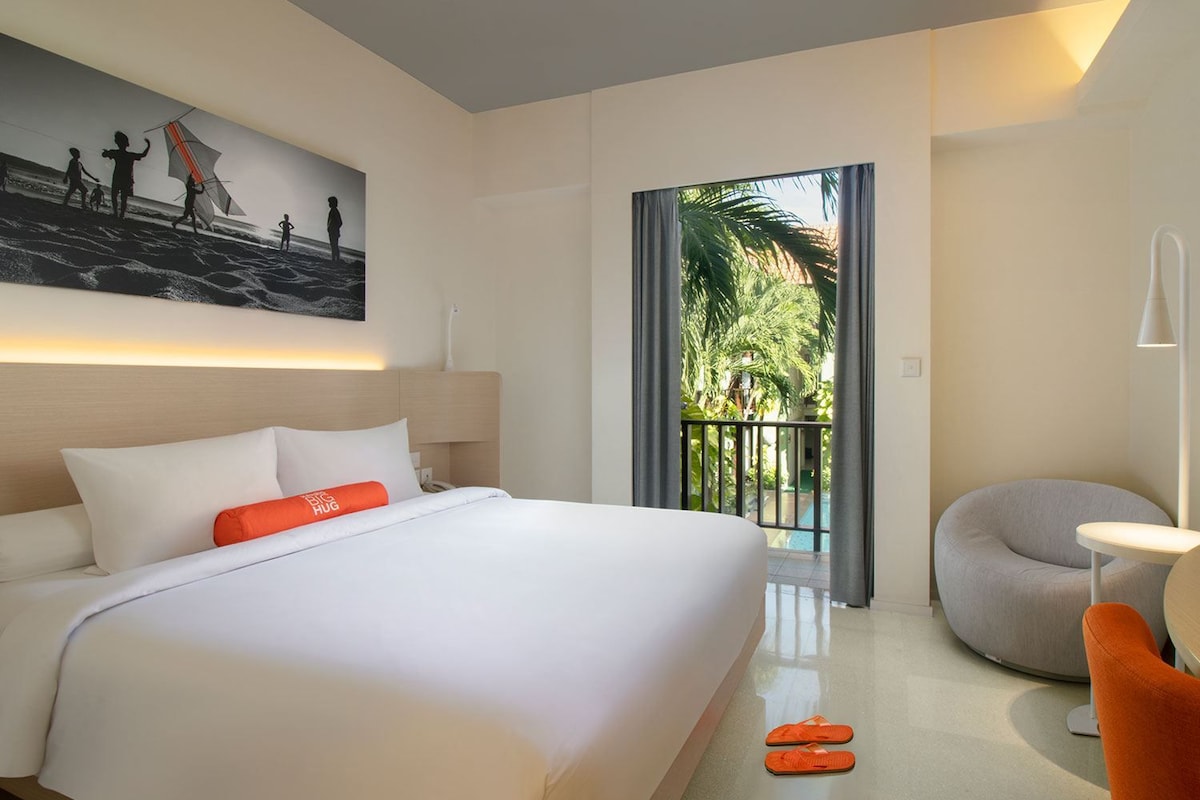 A hotel room with a bed, a painting, a balcony with a view, and a chair.