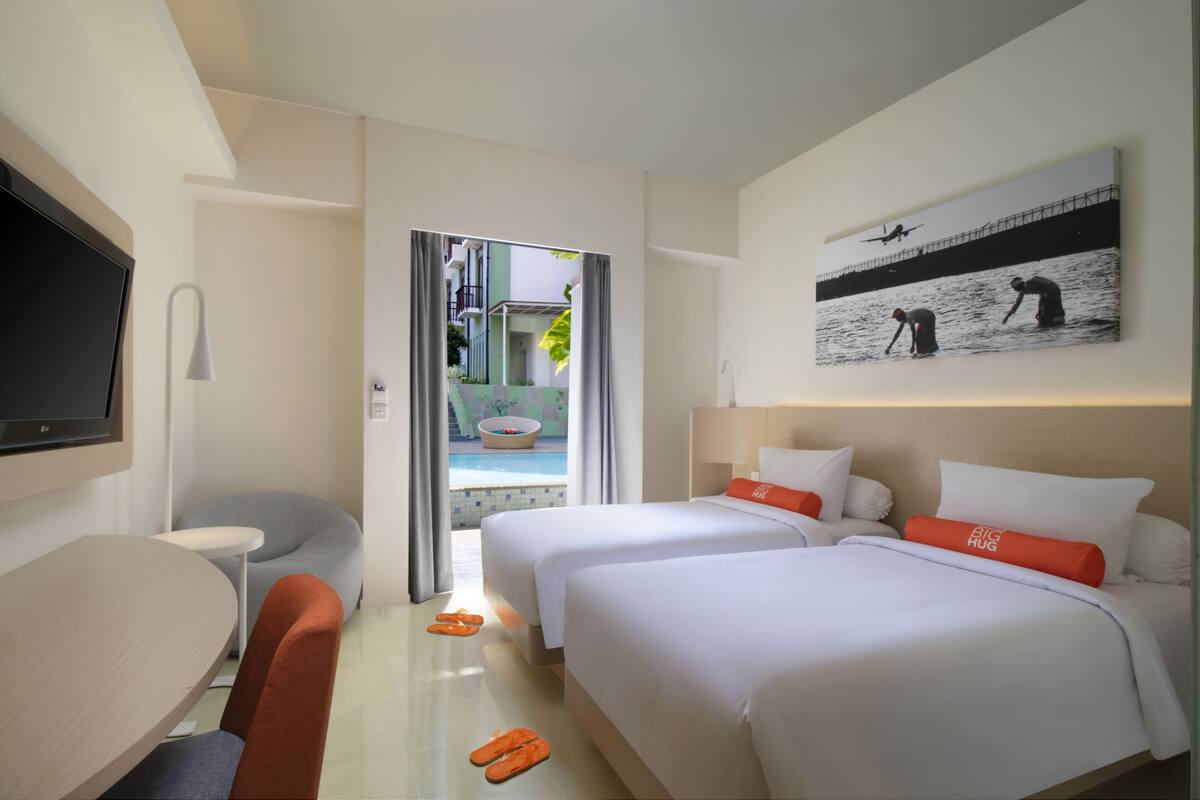 A hotel room with two beds, a TV, a desk, and a view of a pool and outdoor area.