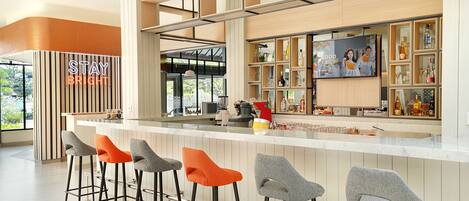 A modern bar area with a long counter, four bar stools, and a television screen displaying an advertisement.