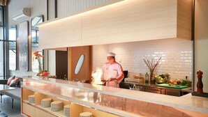 A modern kitchen with a chef preparing food, a counter with stacked plates, and a seating area with a bench.