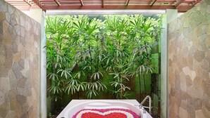 A bathroom with a heart-shaped flower arrangement in the bathtub, surrounded by lush green plants.