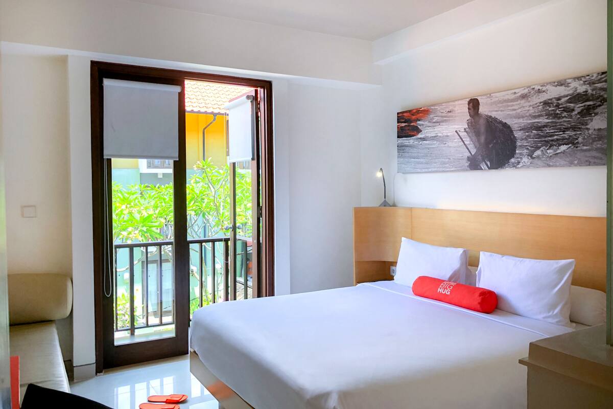 A hotel room with a large bed, a sliding glass door to a balcony, and a painting on the wall.