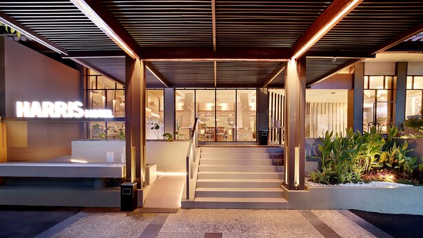 A modern hotel entrance with a staircase leading to the lobby, a visible sign for the Harris Hotel, and a well-lit outdoor area with plants.