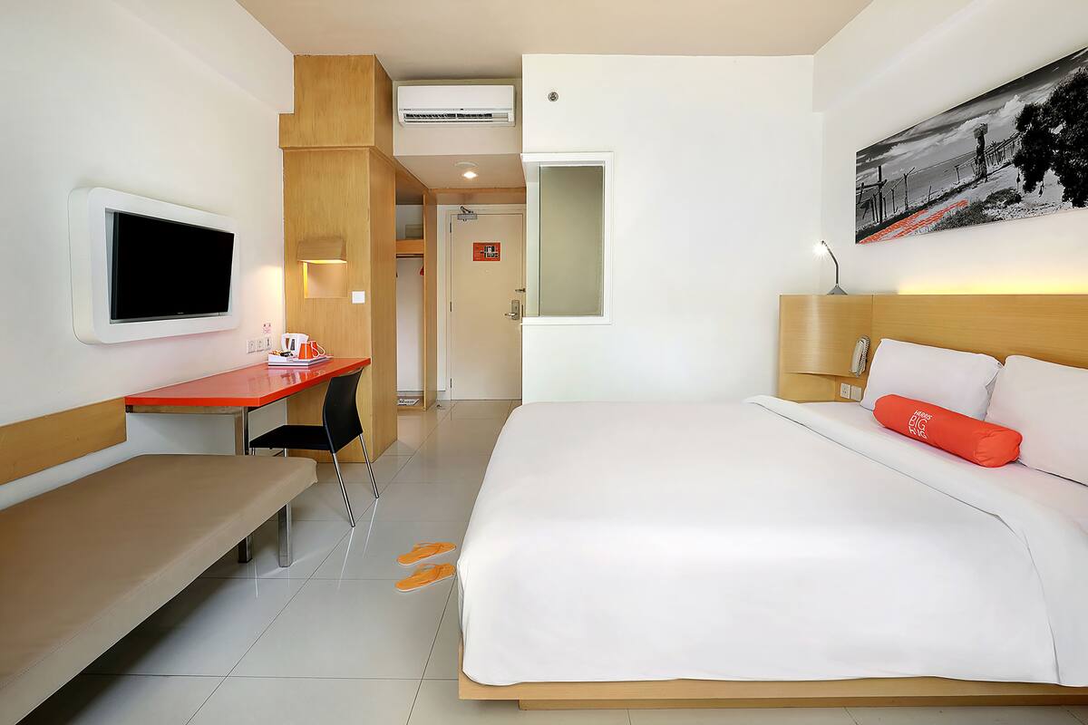 A hotel room with a bed, a desk, a chair, a TV, and a painting on the wall.