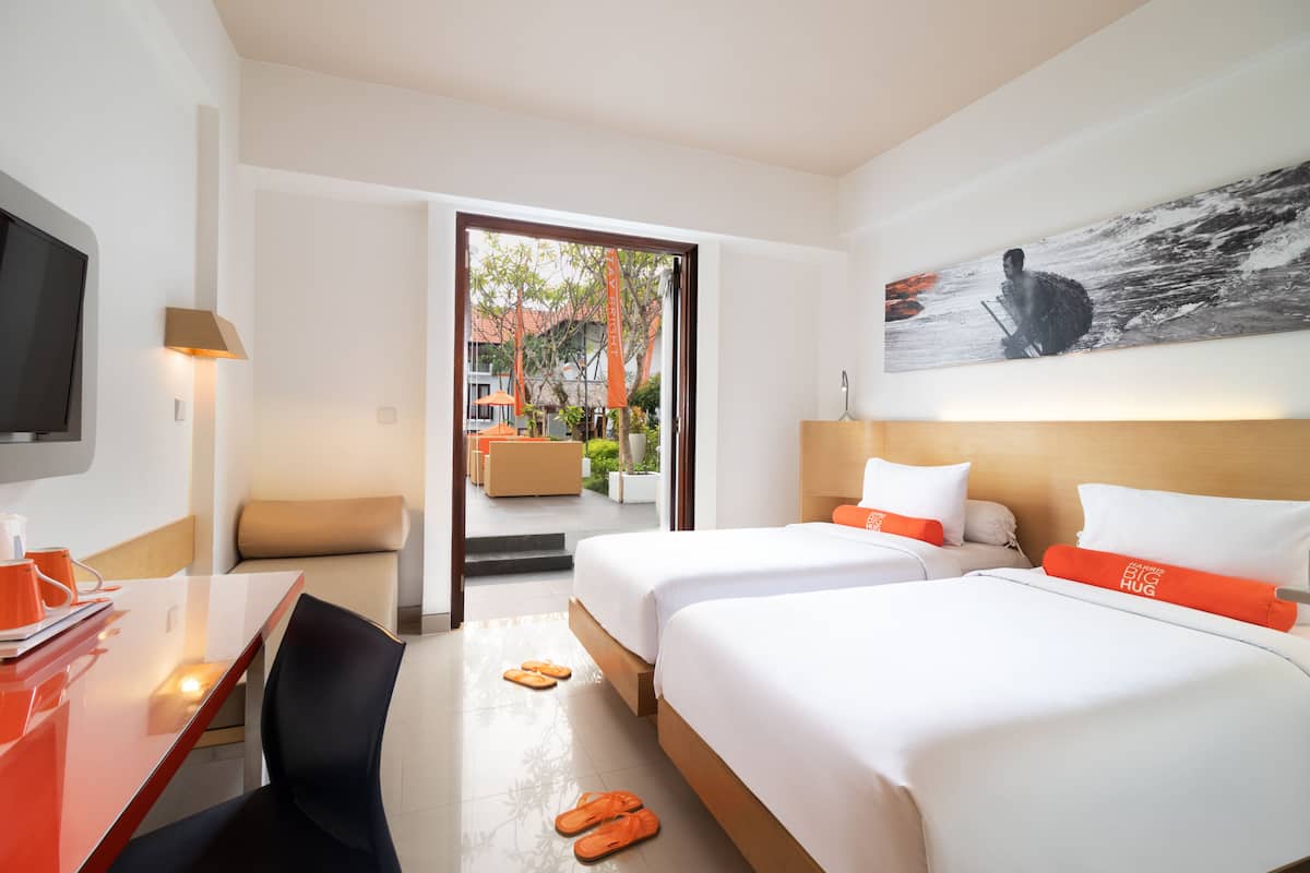 A hotel room with two beds, a desk, a TV, and a view of the outdoor area.