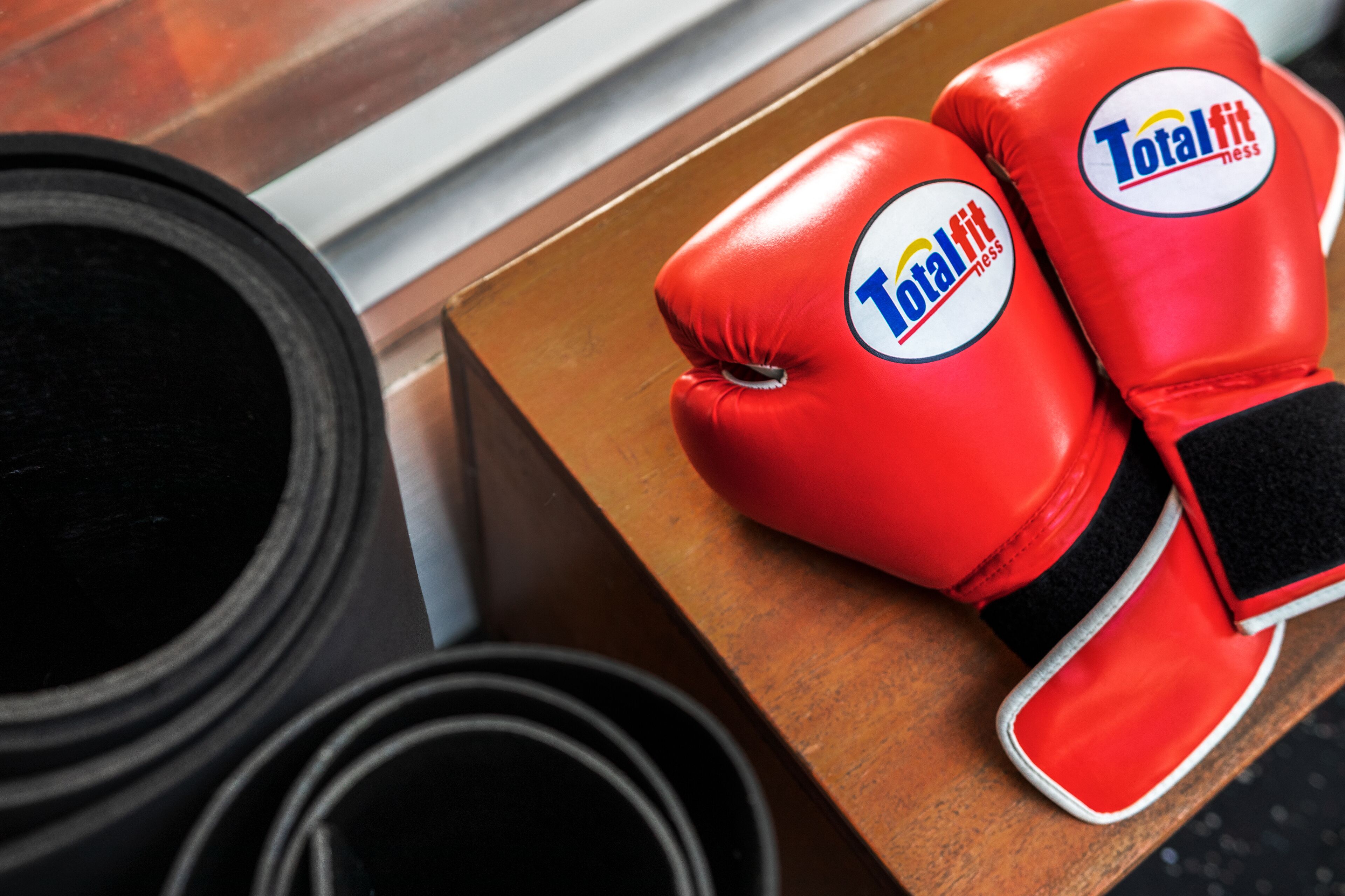 Un par de guantes de boxeo rojos con el logotipo "Total Fit" sobre una superficie de madera.