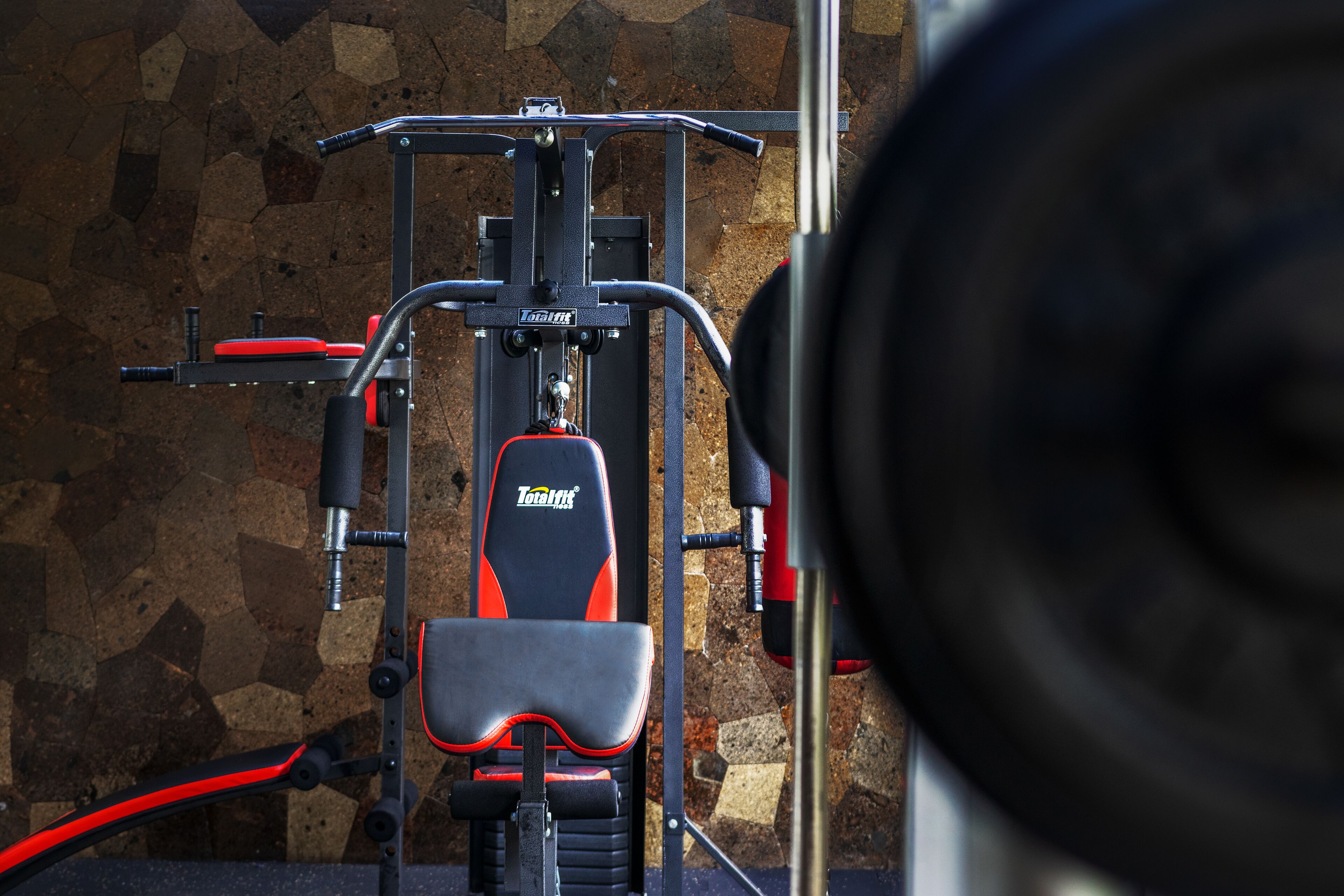 A gym with a TotalFit branded exercise machine, a stone wall background, and a mirror.