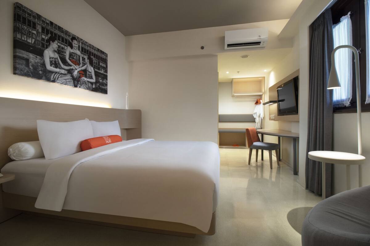 A hotel room with a bed, a desk, a chair, a TV, and a painting on the wall.