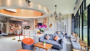 A modern hotel lobby with a curved reception desk, seating area with sofas and armchairs, a wooden accent wall, and a large window offering a view.