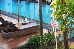 Zona de piscina con una silla de mimbre, una mesita con una planta y un cartel con números de teléfono.
