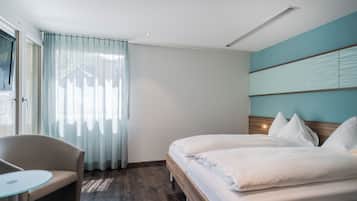 Quarto de hotel com cama, uma cadeira, uma mesinha e janela com cortinas.