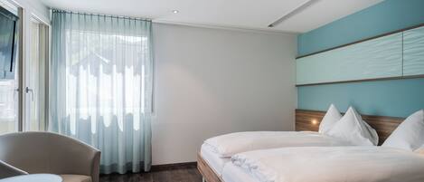 Una habitación de hotel con cama, una silla, una mesita y una ventana con cortinas.