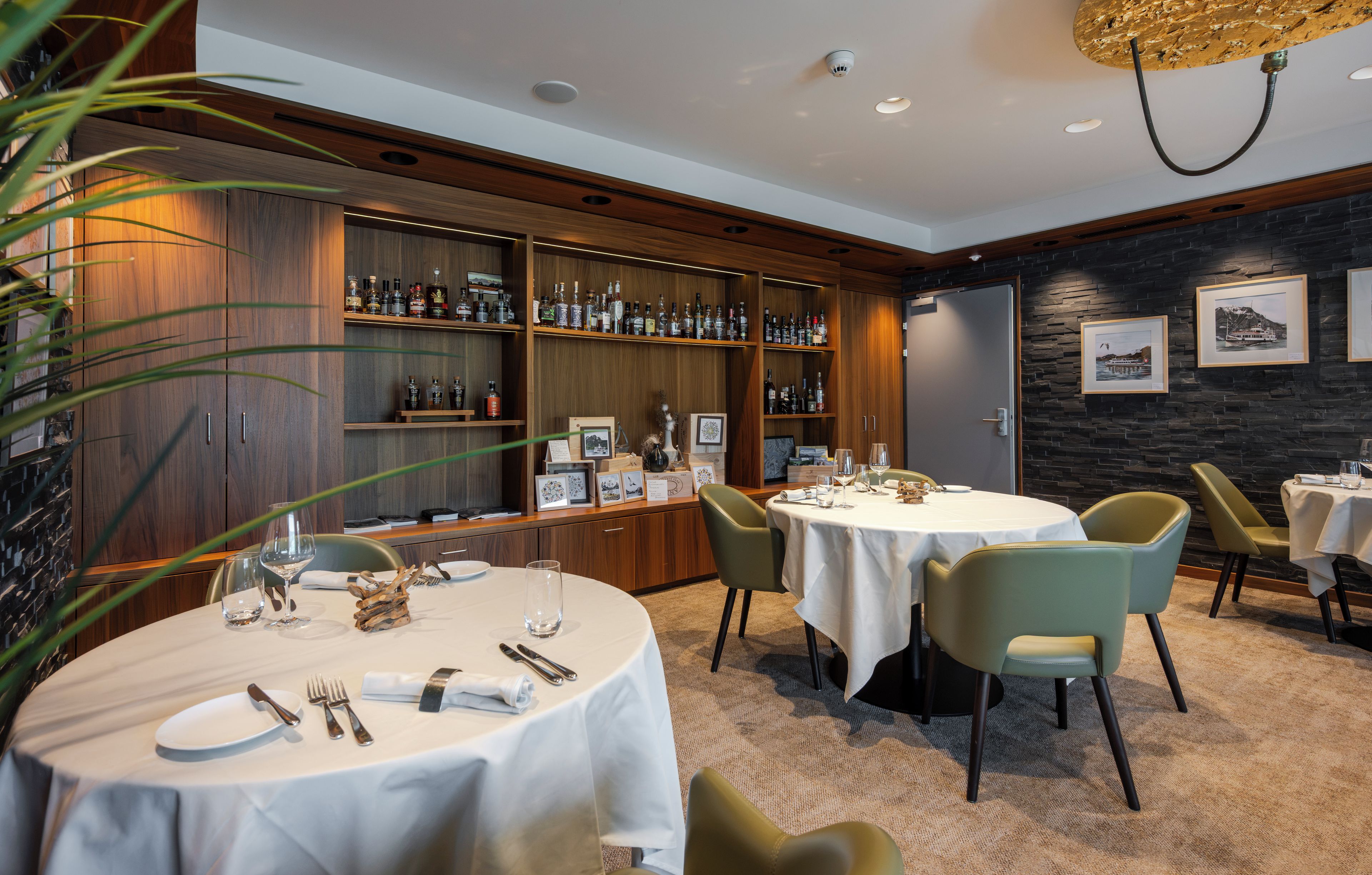 Un restaurant avec des tables rondes, des chaises et un bar doté d’étagères remplies de bouteilles.